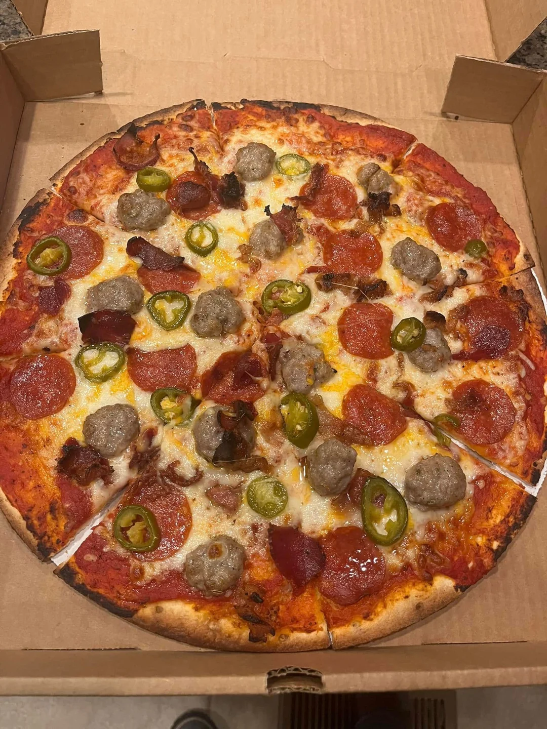 Pizza with cheese, meat toppings and green pepper rings in an open box