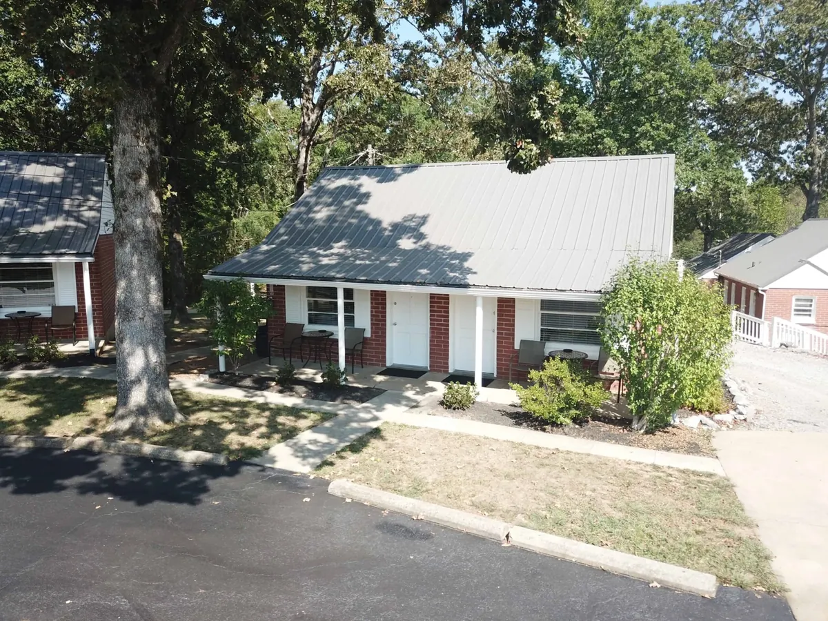 A red-brick cabin and its porch beneath mature shade trees at Early American Motel