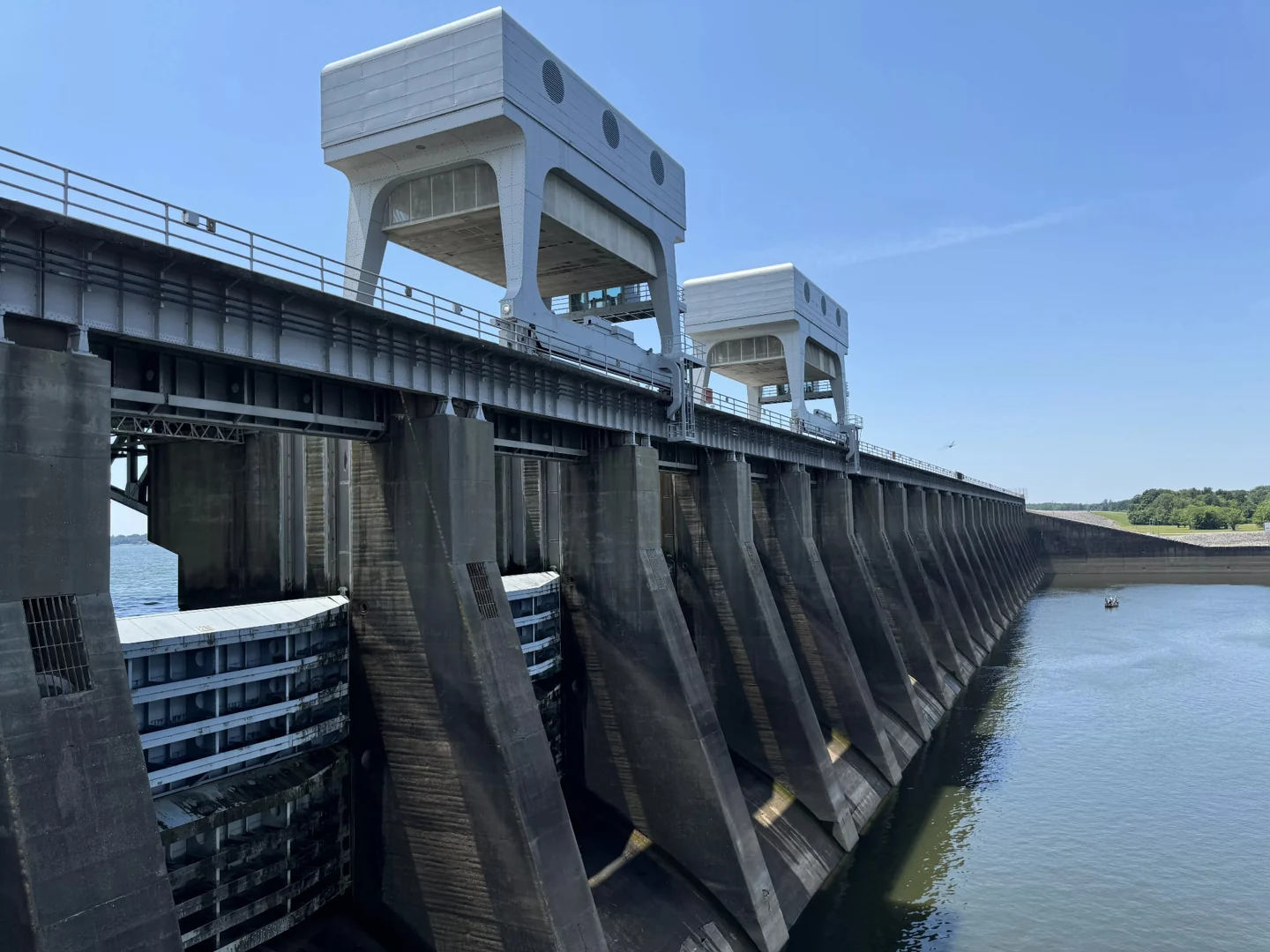 Concrete dam spillway with steel gates and lifting structures beside the water.